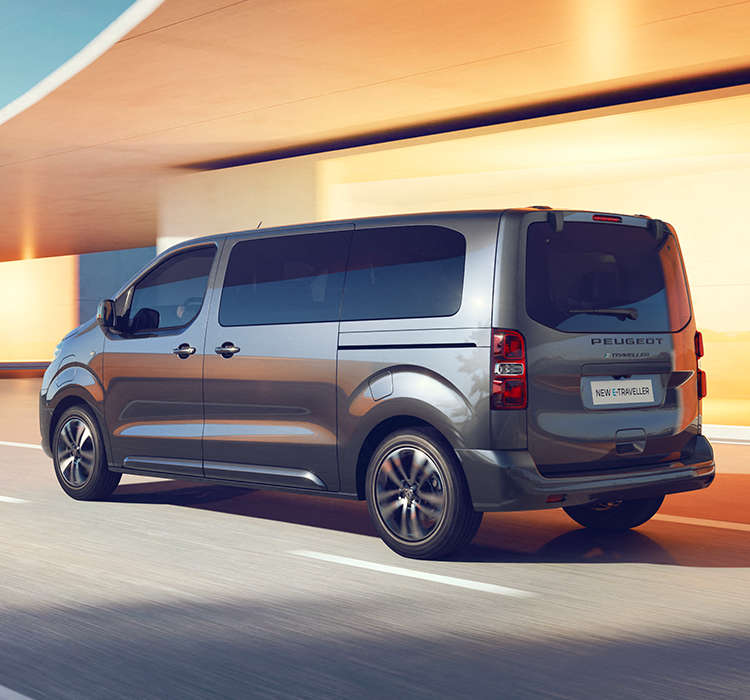 Peugeot Traveller їде по дорозі, вигляд ззаду з лівого боку
